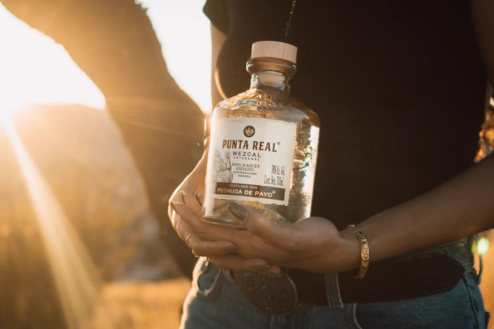 Botella de Punta Real sostenida al atardecer en el campo